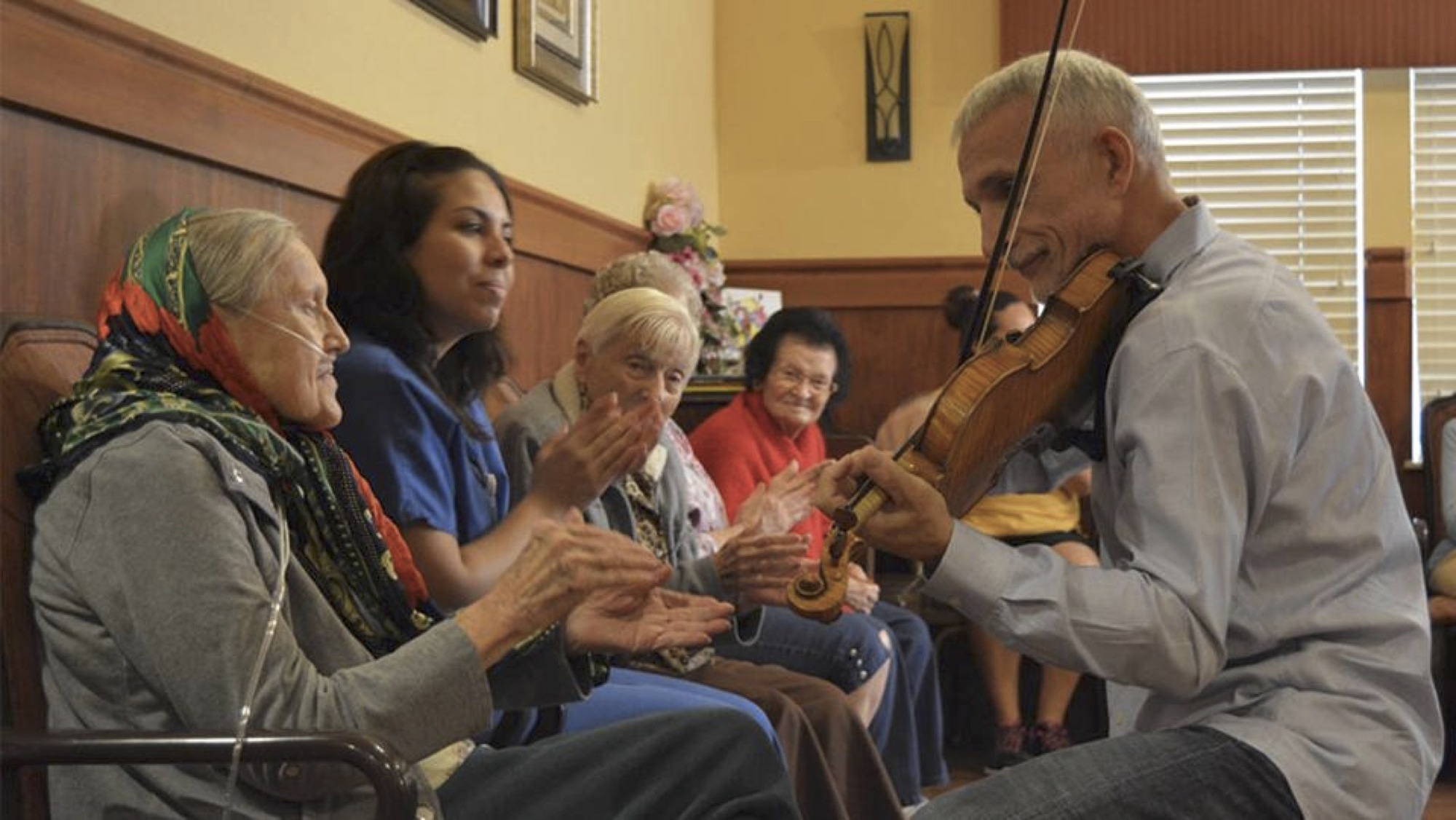 Person playing violin for small group of elderly people